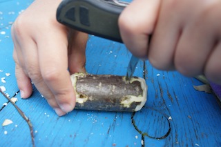 Unsere kleinen Holzschnitzer bohren mit der Ahle (Dorn vom Taschenmesser für Kinder) vier Löcher auf eine Seite des großen Stück Holzes. Foto. (c) Kinderoutdoor.de